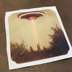 May include: A vintage-style photograph of a flying saucer hovering over a group of people in a forest. The saucer is glowing red and white, and the people are silhouetted against the sky.