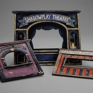 May include: Three antique-style shadow play theater frames. The largest is navy blue with "SHADOWPLAY THEATRE" text. The other two are smaller, one purple with "MADAME MOTH" and the other red and black with "Sideshow Curiosities".
