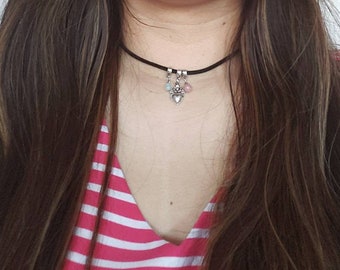 May include: A black choker necklace with a silver heart charm and two small pink and blue beads hanging from it.