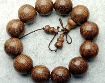 May include: A wooden beaded bracelet with brown beads and a decorative wooden charm. The bracelet is made of natural wood and has a rustic look.