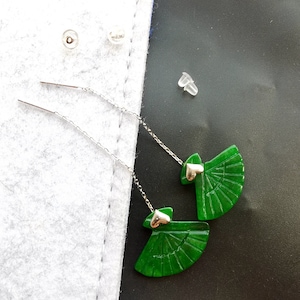 Peut inclure: Une paire de boucles d'oreilles en jade vert en forme d'éventail avec un charme en forme de cœur argenté. Les boucles d'oreilles sont sur une chaîne argentée et sont livrées avec une paire de dos de boucles d'oreilles en silicone transparent.
