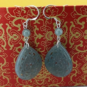 Peut inclure: Une paire de boucles d'oreilles pendantes en argent avec des pendentifs en jade gris en forme de larme. Les pendentifs présentent des motifs sculptés complexes.