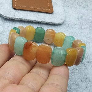 May include: A bracelet made of smooth, oval-shaped stones in shades of green, yellow, and orange. The bracelet is made of natural stones and is a beautiful example of handmade jewelry.