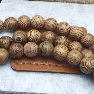 Puede incluir: Primer plano de cuentas de madera con un patr&oacute;n a rayas en tonos marrones y beige. Las cuentas redondas est&aacute;n dispuestas sobre una superficie de cuero marr&oacute;n, lo que sugiere un tema artesanal o de joyer&iacute;a.