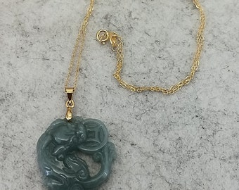 Puede incluir: Un collar con un colgante de jade verde tallado con un diseño de dragón. El colgante está unido a una cadena de oro.