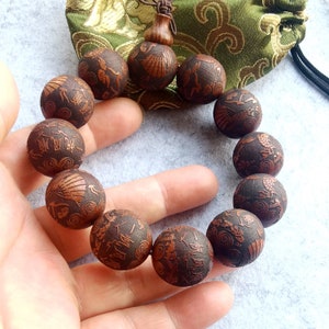 May include: A brown wooden bracelet with intricate carvings of Chinese characters and designs. The bracelet is made of 18 beads and has a tassel at the end.