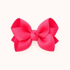 May include: A bright hot pink hair bow constructed from ribbed grosgrain ribbon. The accessory features a central knot with two symmetrical loops on each side, creating a classic bow shape with a textured, horizontally lined fabric surface.