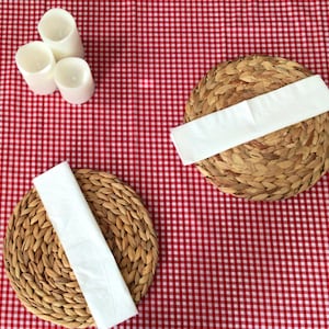 May include: Two woven placemats with white napkins on a red and white gingham tablecloth. The placemats are round and made of natural materials.