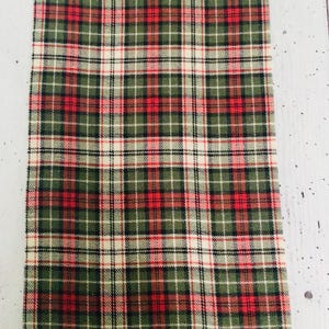 May include: A rectangular fabric with a traditional tartan pattern. The design incorporates a grid of intersecting lines in red, green, black, and white. The fabric is suitable for home decor or craft projects.
