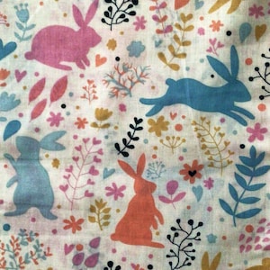 May include: A white fabric with a repeating pattern of colorful bunnies, flowers, and foliage. The bunnies are in shades of pink, blue, orange, and yellow. The floral elements include pink, yellow, and blue flowers, with green and black foliage.