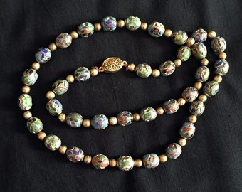 May include: A gold necklace with colorful enamel beads. Each bead is decorated with a floral pattern in shades of blue, green, red, and white.