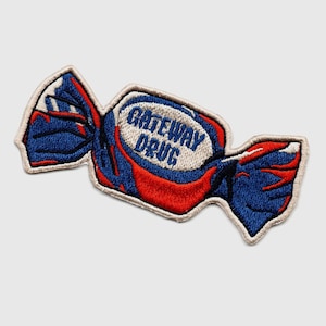 Puede incluir: Un parche bordado con forma de caramelo con el texto "GATEWAY DRUG" en el caramelo. El parche es azul y rojo.
