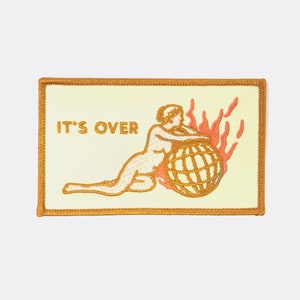 May include: A yellow embroidered patch with a woman holding a globe on fire. The text "IT'S OVER" is written in the top left corner.