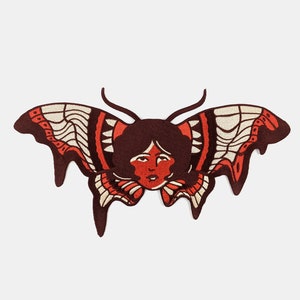 Puede incluir: Una mariposa roja y blanca con la cara de una mujer en el centro. La mariposa tiene un efecto de goteo y está delineada en marrón.