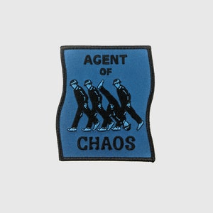 Op de afbeelding: Blauwe geborduurde patch met de tekst "AGENT OF CHAOS" en een afbeelding van vier zwarte figuren die in een rij lopen.