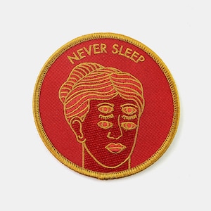 Puede incluir: Parche bordado rojo con contorno dorado. El parche presenta una cara estilizada con múltiples ojos y el texto "NEVER SLEEP".