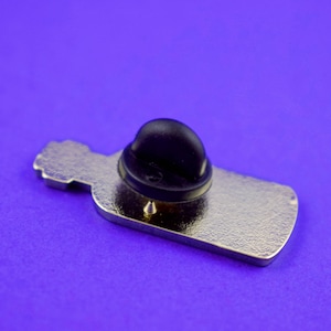 May include: The back of a silver metal bottle pin with a black rubber pin back.