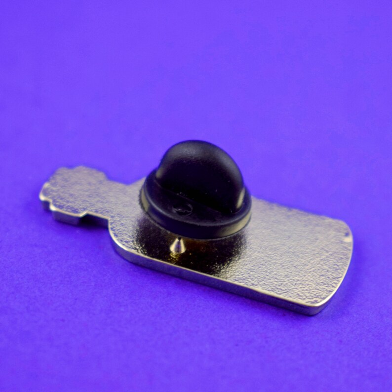 May include: The back of a silver metal bottle pin with a black rubber pin back.