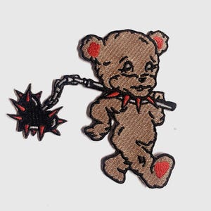 Puede incluir: Parche bordado con un oso de peluche marrón con detalles rojos, sosteniendo una maza negra con púas rojas. El parche tiene un estilo de dibujos animados y un diseño ligeramente agresivo, adecuado para ropa o accesorios.