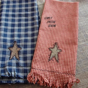 May include: Two tea towels, one blue and white plaid with a brown star, and one red and white gingham with a brown star. The red and white towel has the text "Simply Special Sewing" embroidered on it.