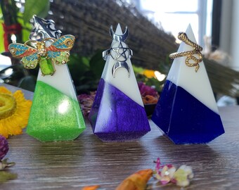 May include: Three pyramid-shaped ring holders. One is green with a butterfly, one is purple with a crescent moon, and one is blue with a snake. Each has a white top and a diagonal color split.