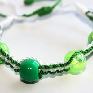 May include: A green and white braided bracelet with green beads. The bracelet is made with a knotting technique.