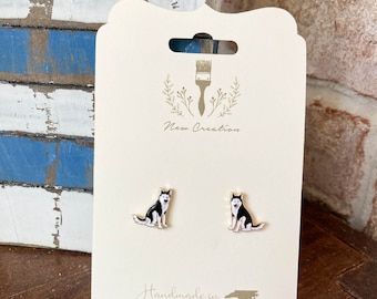 May include: A pair of gold stud earrings featuring a black and white husky dog design. The earrings are displayed on a white card with the text "New Creation" and "Handmade in NC".