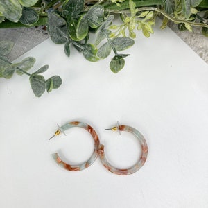 May include: A pair of hoop earrings with a marbled design in shades of blue, white, and brown.