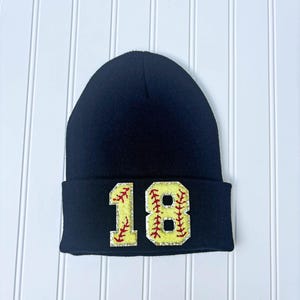 May include: Black beanie with a yellow and red softball design and the number 18.