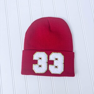 May include: Red knit beanie with a white felt number 33 on the front. The number has a gold outline.
