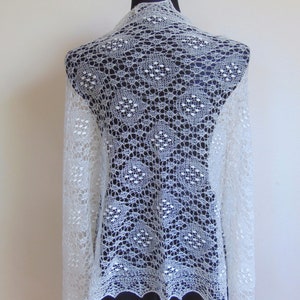 May include: White lace shawl with a delicate pattern. The shawl is draped over a black mannequin.