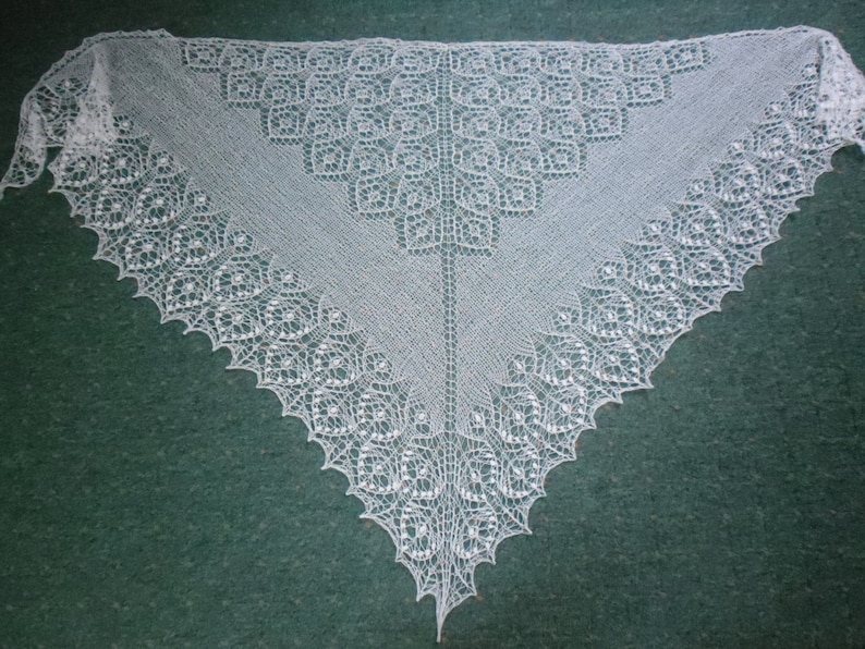 May include: A white crocheted shawl with a delicate lace pattern. The shawl is triangular in shape and has a scalloped edge.