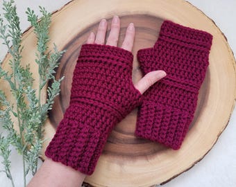 May include: A pair of maroon crocheted fingerless gloves with a ribbed cuff. The gloves are on a wooden surface.