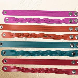 May include: A collection of colorful leather bracelet straps in shades of pink, orange, teal, and red. Some straps are braided, while others are smooth. Each strap has metal snap closures.