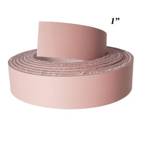 Op de afbeelding: Een rol blush-kleurige leren strip, ongeveer 2,5 cm breed, wordt getoond tegen een witte achtergrond. Het leer is strak opgerold, met een uitgerold gedeelte om de dikte en textuur van het materiaal te laten zien. De afbeelding benadrukt het gladde oppervlak van het leer.