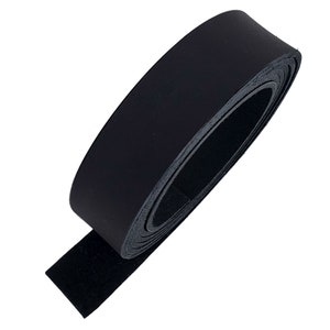 May include: A roll of black leather strip, tightly coiled. The leather has a smooth, shiny surface on one side and a textured, suede-like finish on the other. The strip is unrolled at the end, revealing the suede side.