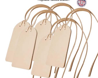 May include: Several large, blank leather luggage tags, each approximately 4 inches by 2 inches, with attached leather straps. The tags are a light tan color and are made from vegetable-tanned leather. The text "Large Leather Luggage Tags" and "Made in the USA" are visible.