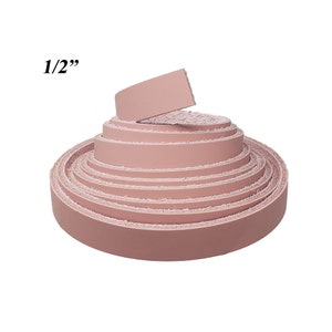 Op de afbeelding: Een rol roze leren stroken, elk ongeveer 1,27 cm breed, wordt weergegeven tegen een witte achtergrond. Het leer is strak opgerold, met de uiteinden van de stroken zichtbaar. De tekst "1/2" staat in de linkerbovenhoek.