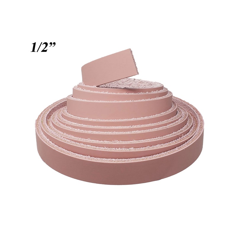 Op de afbeelding: Een rol roze leren stroken, elk ongeveer 1,27 cm breed, wordt weergegeven tegen een witte achtergrond. Het leer is strak opgerold, met de uiteinden van de stroken zichtbaar. De tekst "1/2" staat in de linkerbovenhoek.