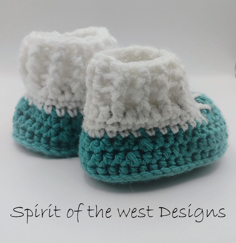 Pu&ograve; includere: Un paio di scarpine da neonato all'uncinetto fatte a mano. Le scarpine hanno una base turchese e un polsino bianco soffice. Il testo "Spirit of the west Designs" &egrave; in basso nell'immagine.