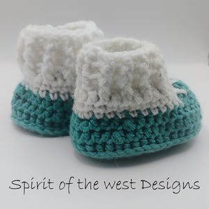 Pu&ograve; includere: Un paio di scarpine da neonato all'uncinetto fatte a mano. Le scarpine hanno una base turchese e un polsino bianco soffice. Il testo "Spirit of the west Designs" &egrave; scritto in corsivo nero nella parte inferiore dell'immagine.