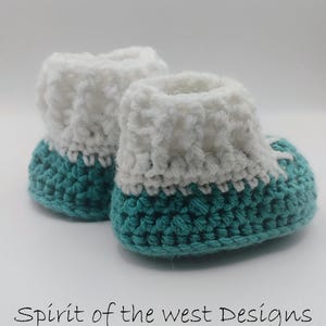 Pu&ograve; includere: Un paio di scarpine da neonato all'uncinetto fatte a mano. Le scarpine hanno una base turchese e un polsino bianco. Il testo "Spirit of the west Designs" &egrave; in basso nell'immagine.