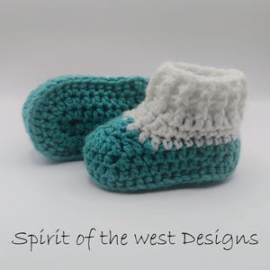Pu&ograve; includere: Scarpine da neonato all'uncinetto fatte a mano in turchese e bianco. Gli stivaletti sono realizzati con un filato morbido e presentano una base turchese e un polsino bianco. Il testo "Spirit of the west Designs" &egrave; in basso nell'immagine.