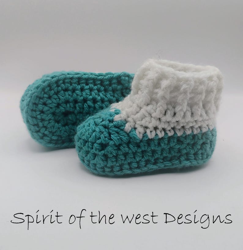 Pu&ograve; includere: Scarpine da neonato all'uncinetto fatte a mano in turchese e bianco. Gli stivaletti sono realizzati con un filato morbido e presentano una base turchese e un polsino bianco. Il testo "Spirit of the west Designs" &egrave; in basso nell'immagine.