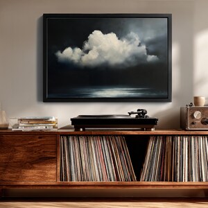 May include: A framed painting of a cloud formation over water, in shades of white, gray, and black, hangs above a wooden cabinet. A black record player sits on top of the cabinet, with a collection of vinyl records stored below.
