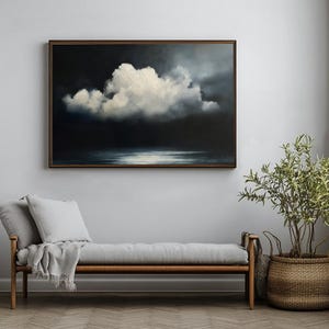 May include: A framed painting of a dramatic cloudscape hangs above a gray bench with pillows and a blanket. A potted plant in a woven basket sits nearby. The artwork features a large white cloud against a dark background.