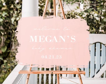 May include: A pink acrylic welcome sign with a white brushstroke design. The sign reads "Welcome to Megan's Baby Shower 04.21.23".