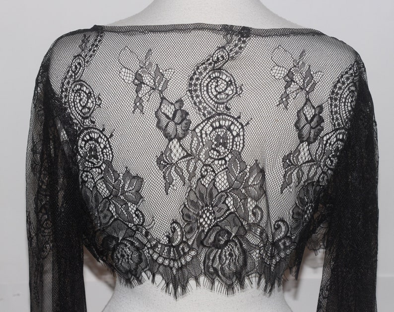 May include: Black lace shrug with long sleeves and a scalloped hem.
