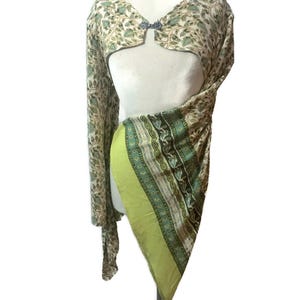 May include: A two-piece garment set featuring a bolero top and a draped skirt. The bolero has a floral pattern in shades of green and beige, with a decorative clasp. The skirt is lime green with patterned borders.