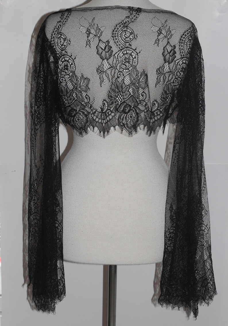 May include: Black lace shrug with long bell sleeves. The shrug is made of delicate lace with a floral pattern.